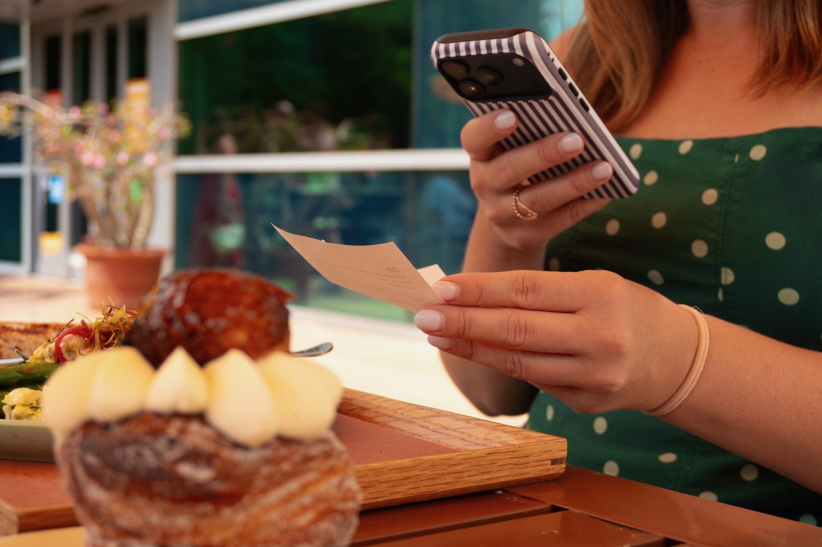 Freelancer reviewing a paper receipt against her phone at a café table.